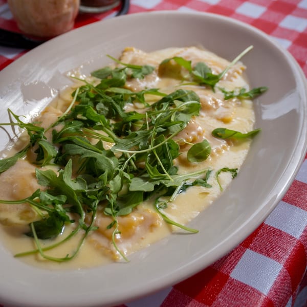 Creamy ravioli topped with fresh arugula on a white plate, resting on a red and white checkered tablecloth.