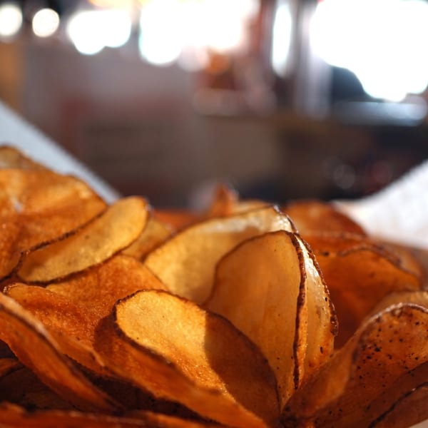 Close-up of crispy, golden-brown potato chips with seasoning, in a basket with a blurred background.