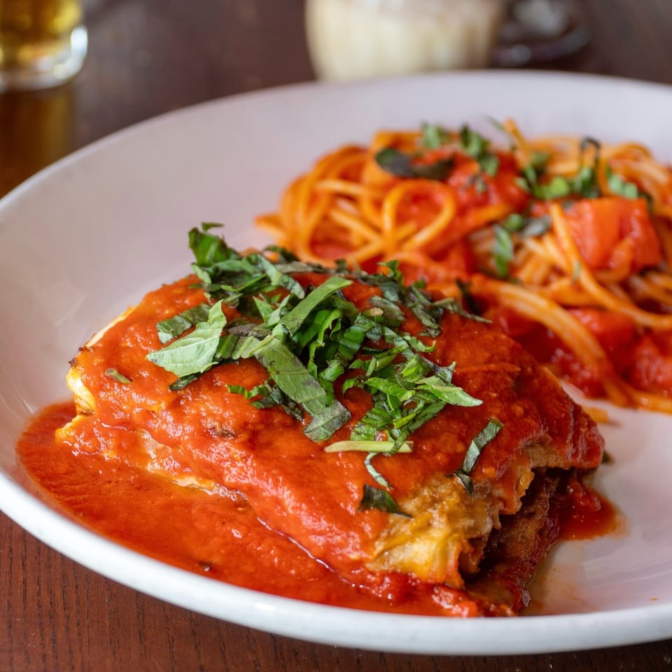 Eggplant parmesan with spaghetti and red sauce, garnished with fresh basil on a white plate.
