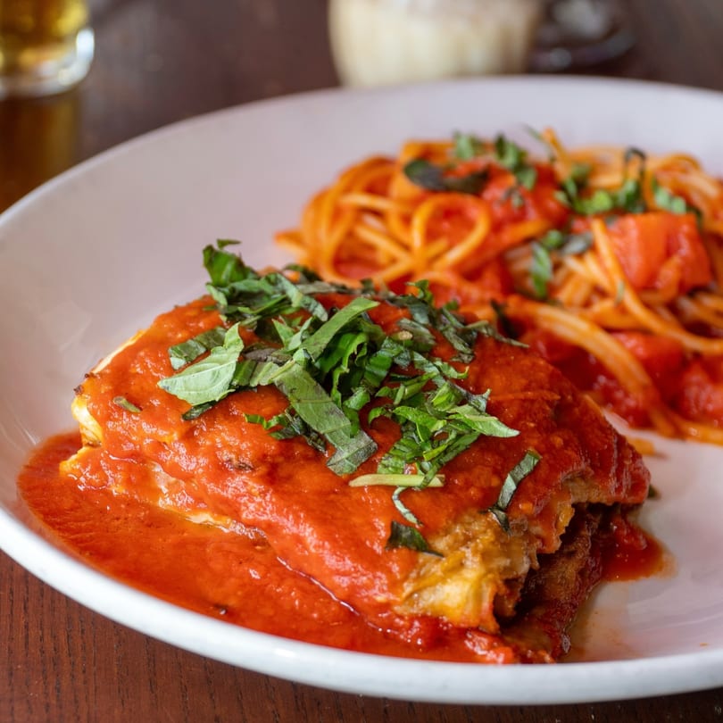 Eggplant parmesan with spaghetti and red sauce, garnished with fresh basil on a white plate.