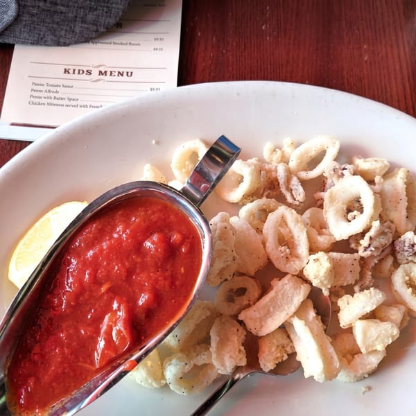 Fried calamari with a side of marinara sauce and a lemon wedge, next to a kids' menu.