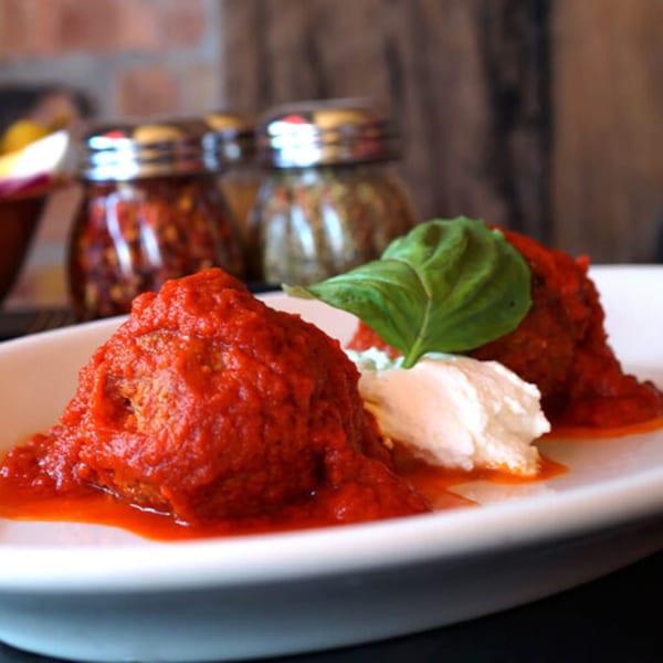 Meatballs in red sauce with a dollop of ricotta cheese and a basil leaf on a white plate.
