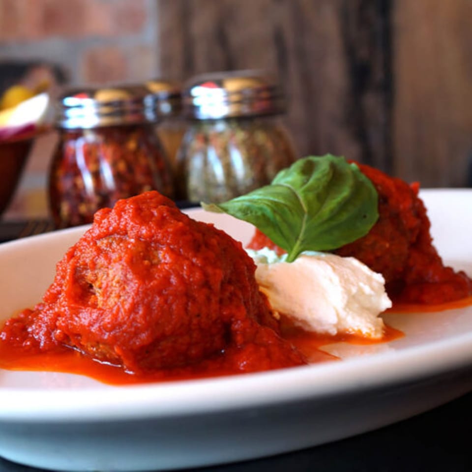Meatballs in red sauce with a dollop of ricotta cheese and a basil leaf on a white plate.