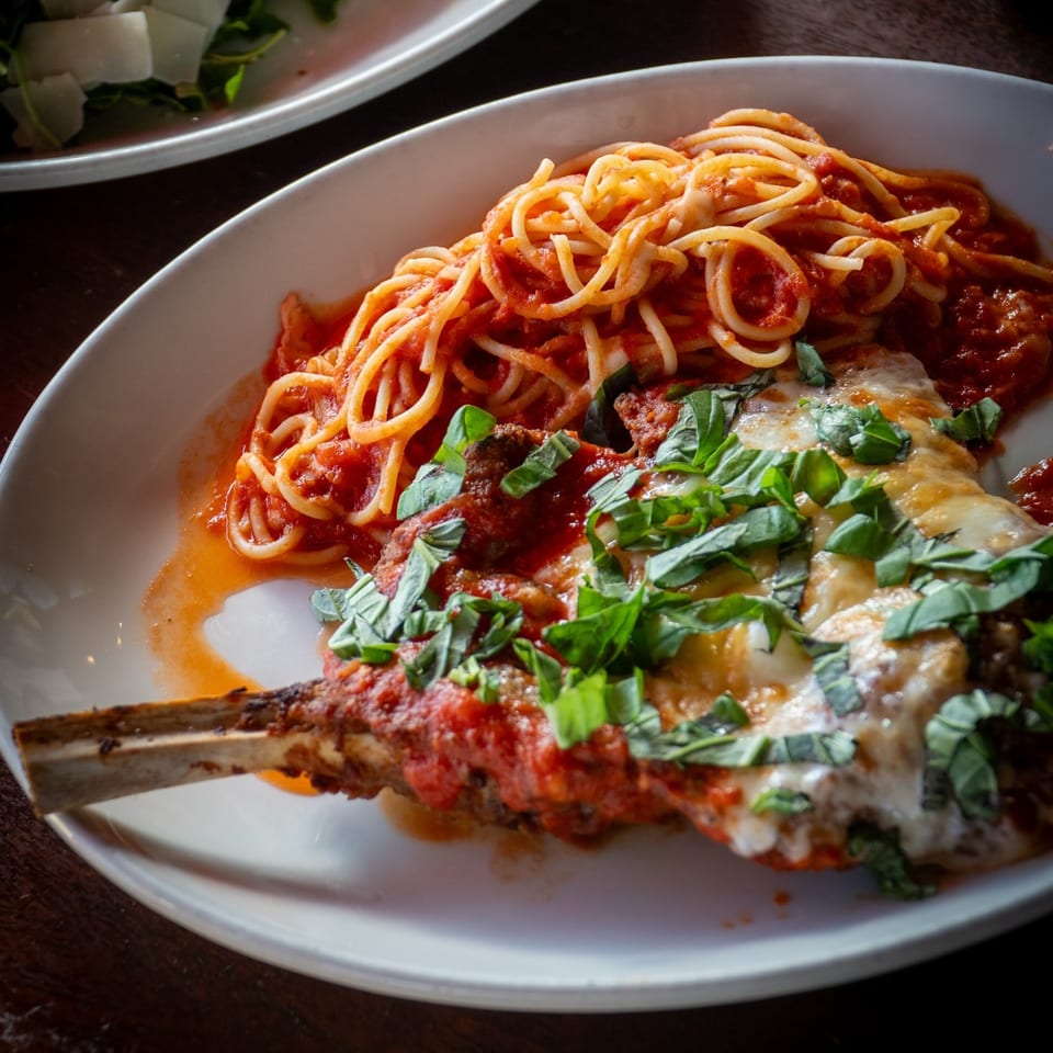 Veal chop parmesan with spaghetti and tomato sauce, garnished with fresh basil on a white plate.