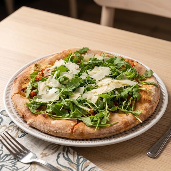 A freshly baked pizza topped with arugula and shaved parmesan cheese on a white plate.
