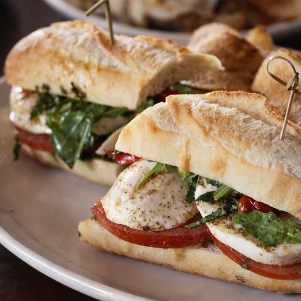 Two fresh caprese sandwiches with mozzarella, tomatoes, and basil on baguettes, served on a white plate.